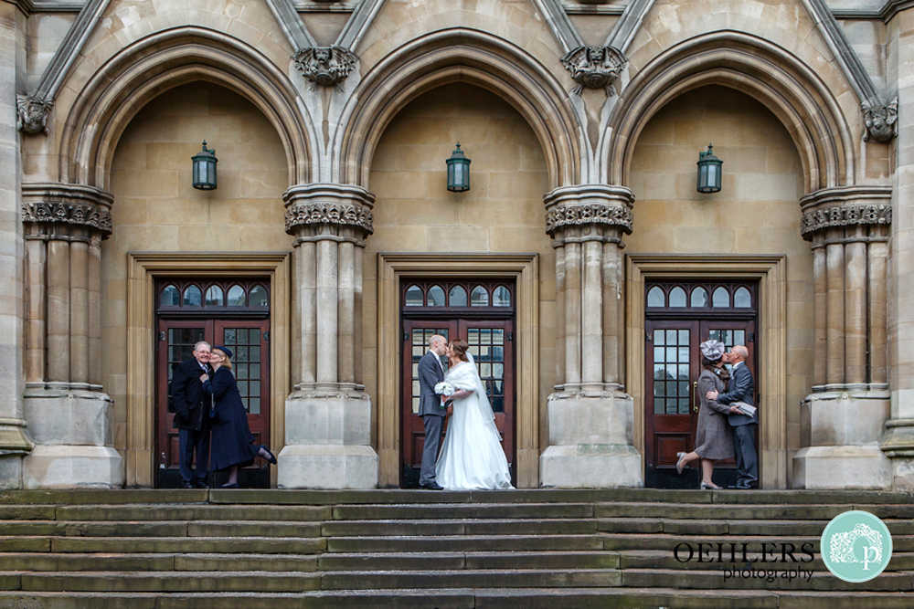 Three archways of building, bride and grrom in middle kissing and their parents on either side kissing