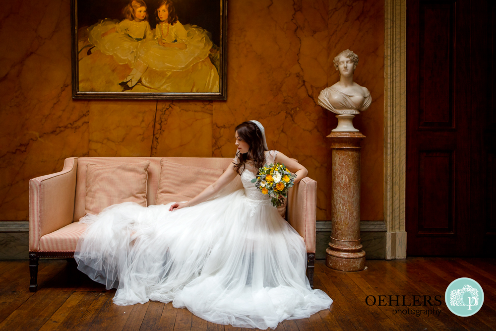 Bride sitting on a sofa adjusting the train of her dress.