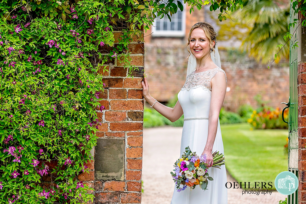 Bride  standing in an archway in the Gardens of Calke Abbey looking directly into the camera.