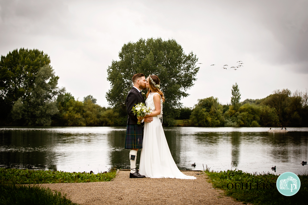 bride and groom kissing at a lake with bird flying in the sky