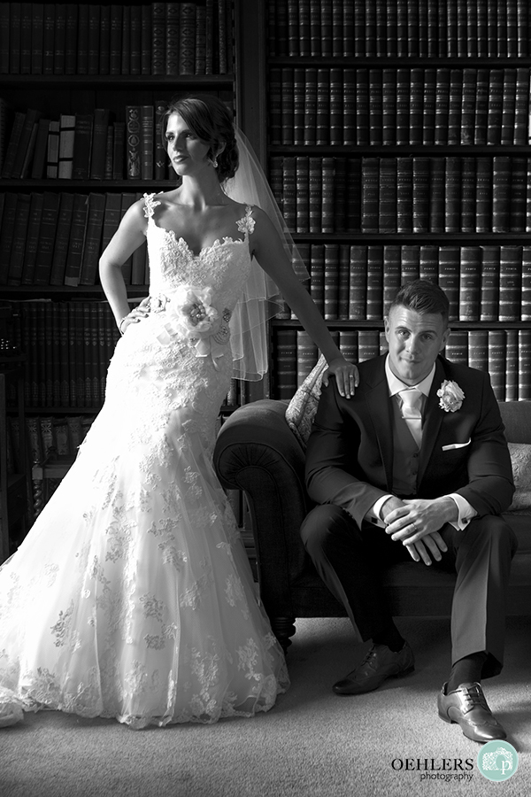 Groom sitting on an armchair whilst bride stands with hand on his right shoulder