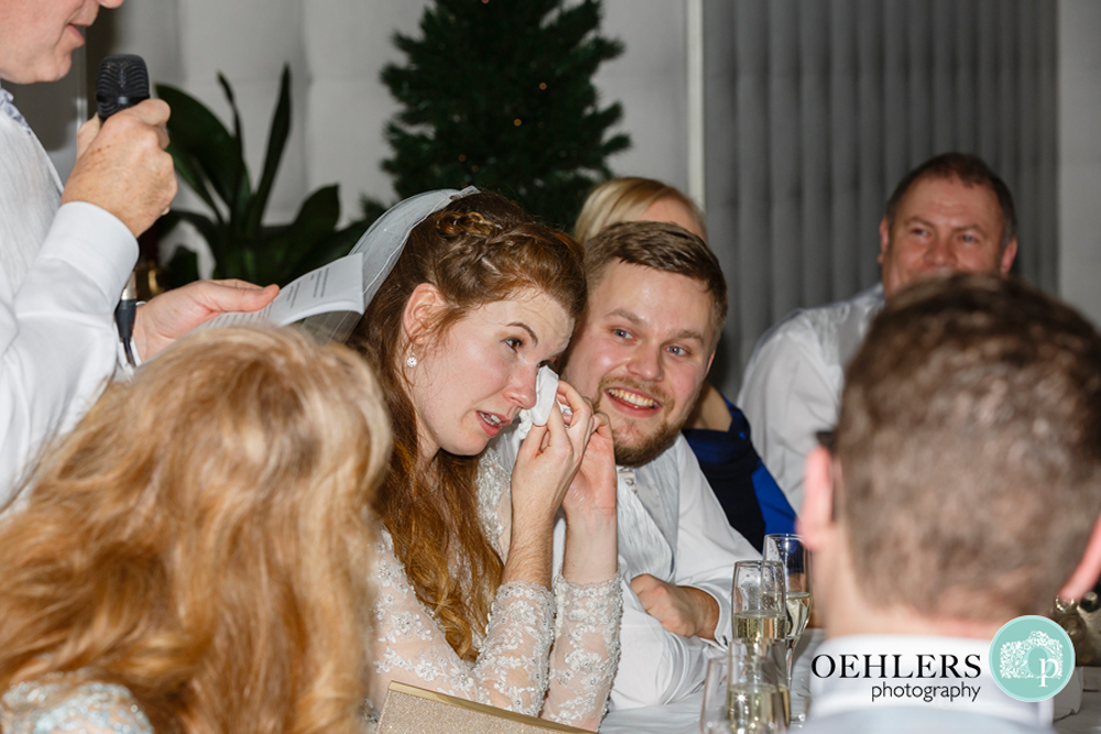 Bride wiping her teary eye whilst her Groom makes a speech