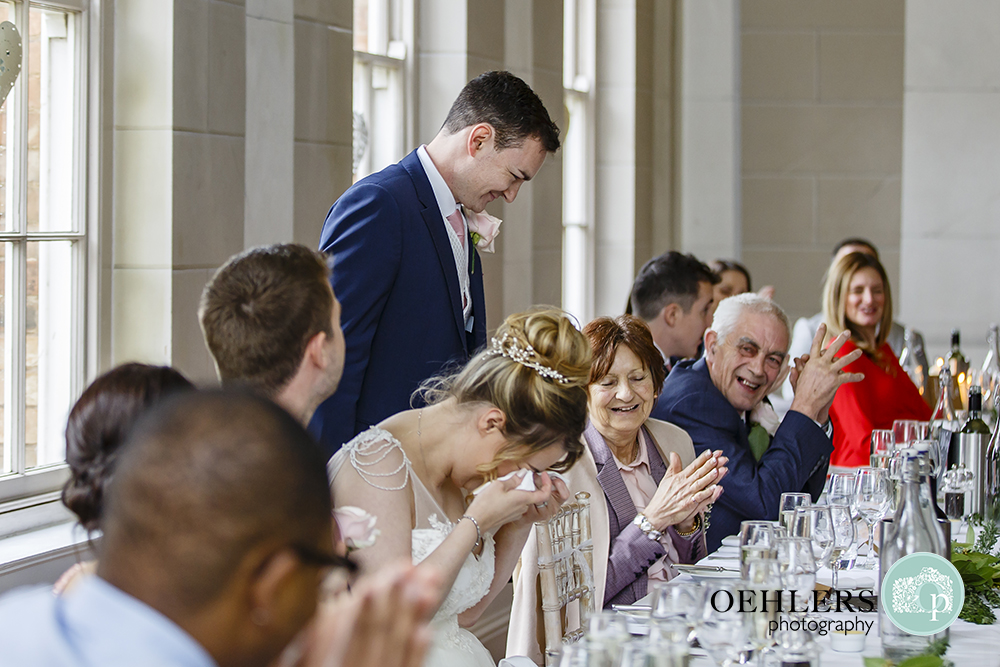 Groom making a funny speech whilst bride cries with laughter