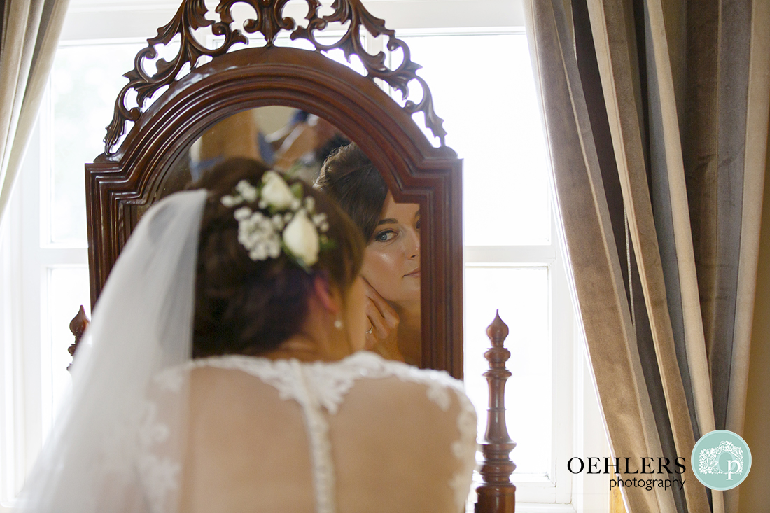 Bride putting on earrings in the mirror