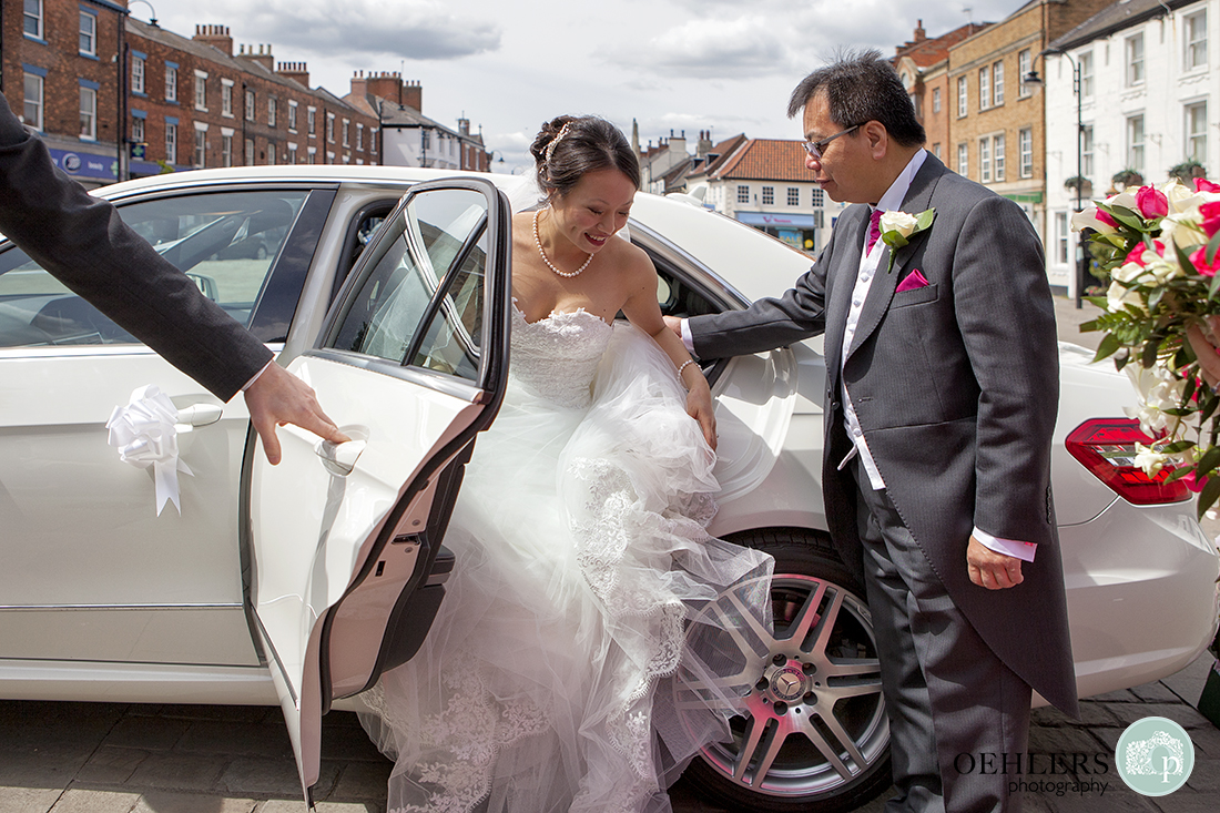 Bride arrives in her wedding car with father helping her out of the car.