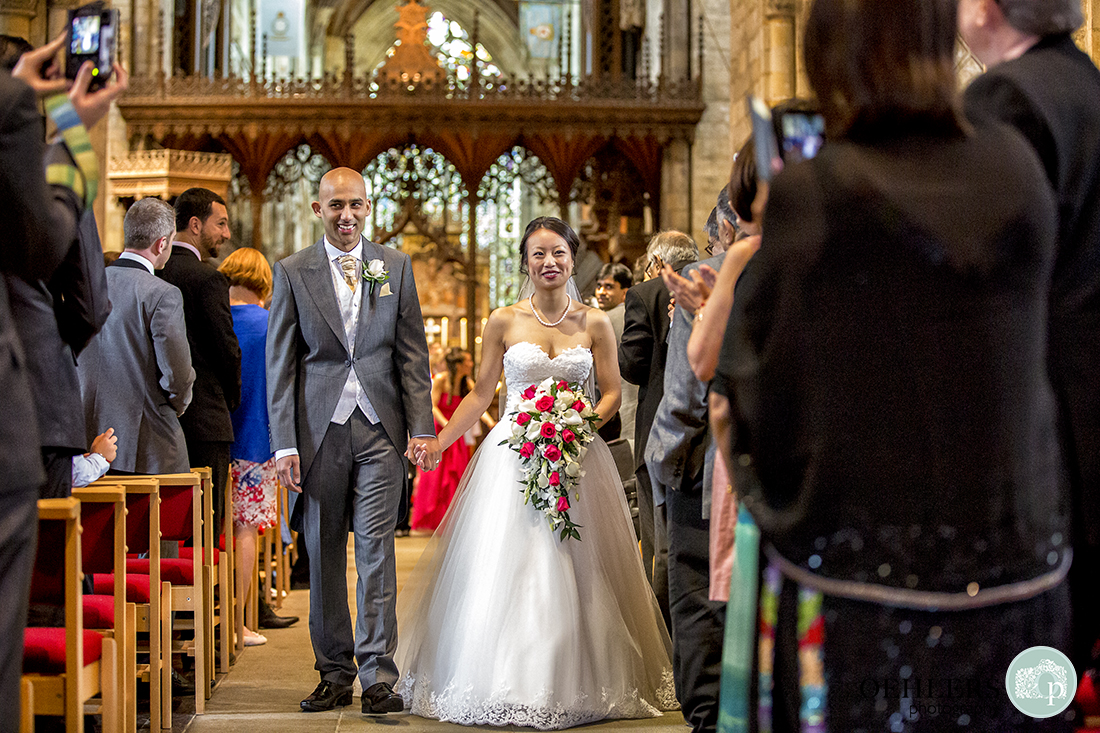 Happy Bride and Groom walking back up the aisle at Selby Abbey whilst the congregation take photographs.