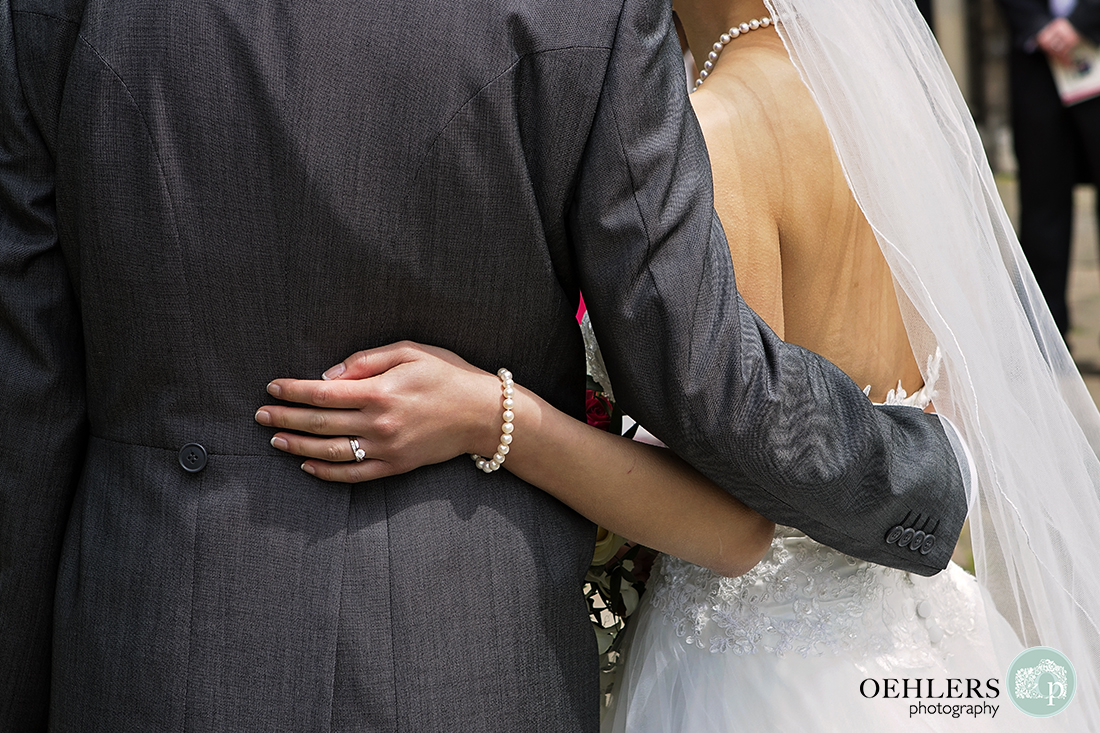 Touching close up photograph of brides hand on the groom's back whilst his arm is around her waist.