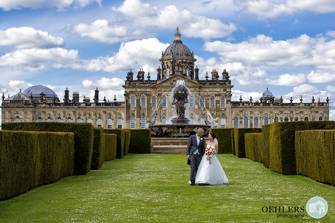 Bride and Groom walking in between yew hedges towards camera with Castle Howard in the backgroud.