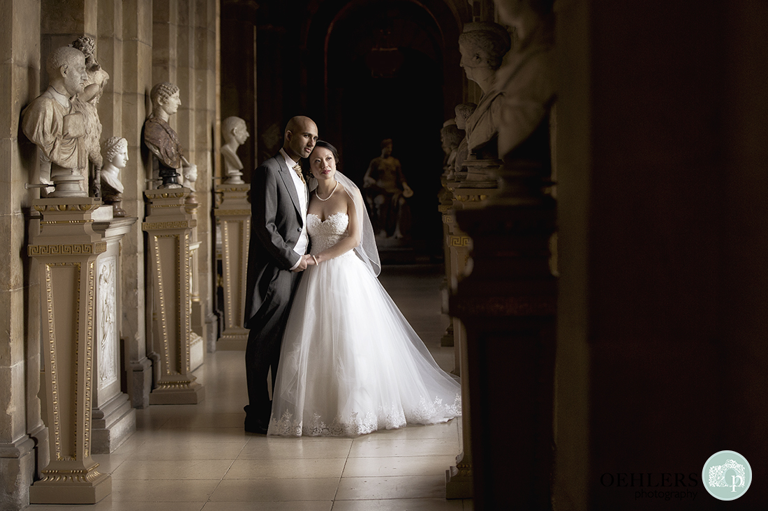 Bride and Groom posing inside the Antique Passage at Castle Howard lined with busts and figurines. 