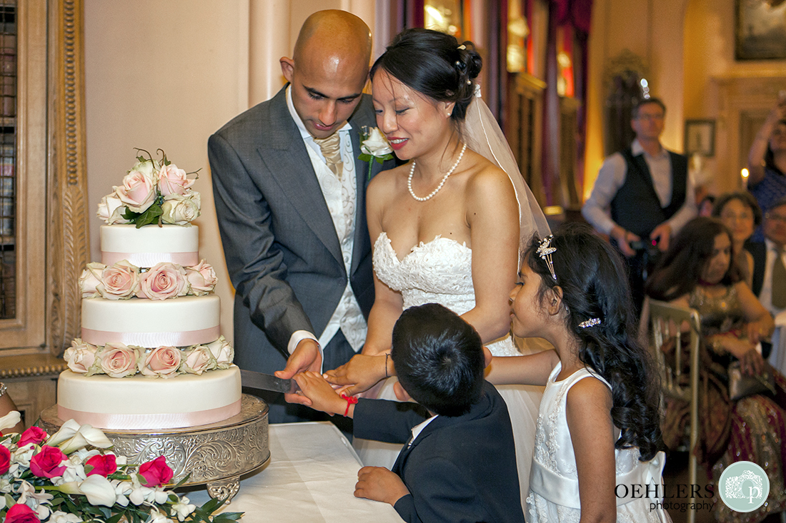 Bride and Groom cutting their wedding cake with flower girl and a boy helping.