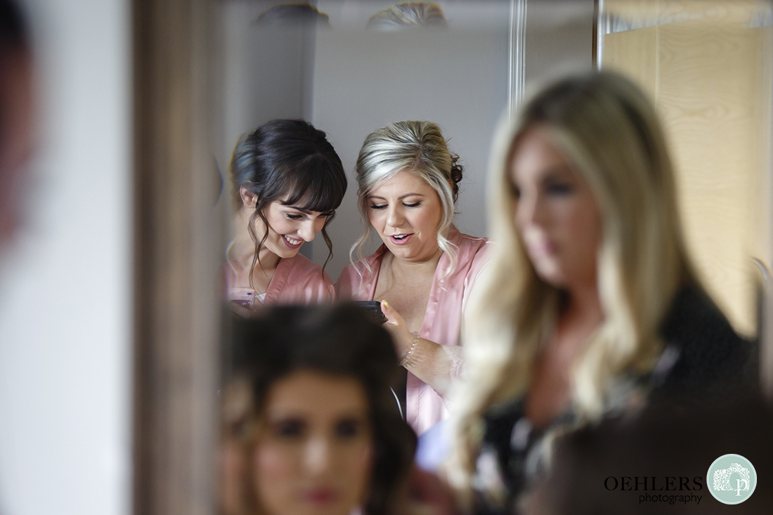 Reflection in mirror of two smiling bridesmaids looking at mobile phones.
