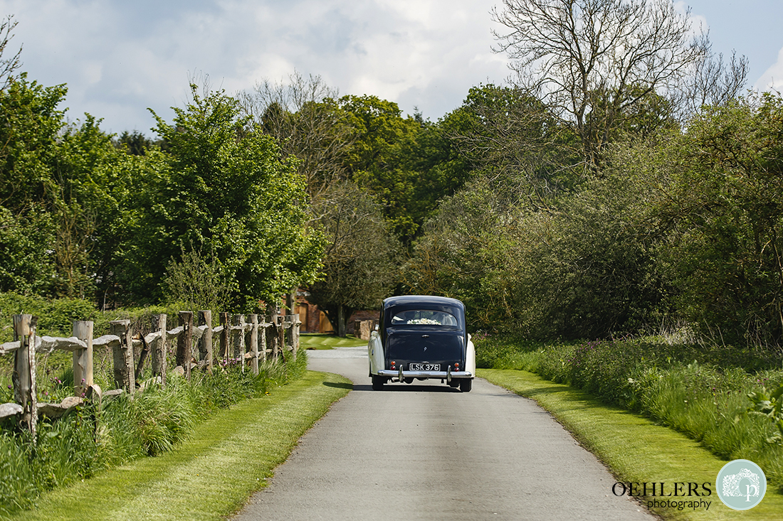 Sleek Rolls-Royce wedding car proceeding along manicured driveway to the venue.