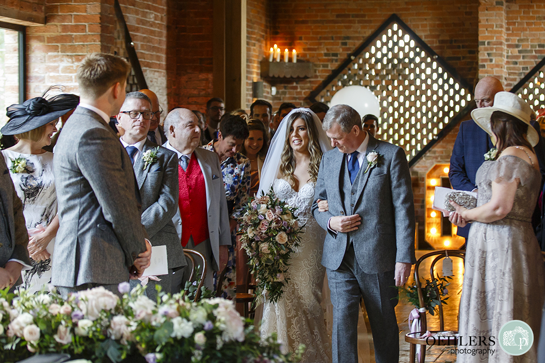 Shustoke Barn Wedding Photographers-Beautiful bride walking down the aisle with father as groom and guests look on.