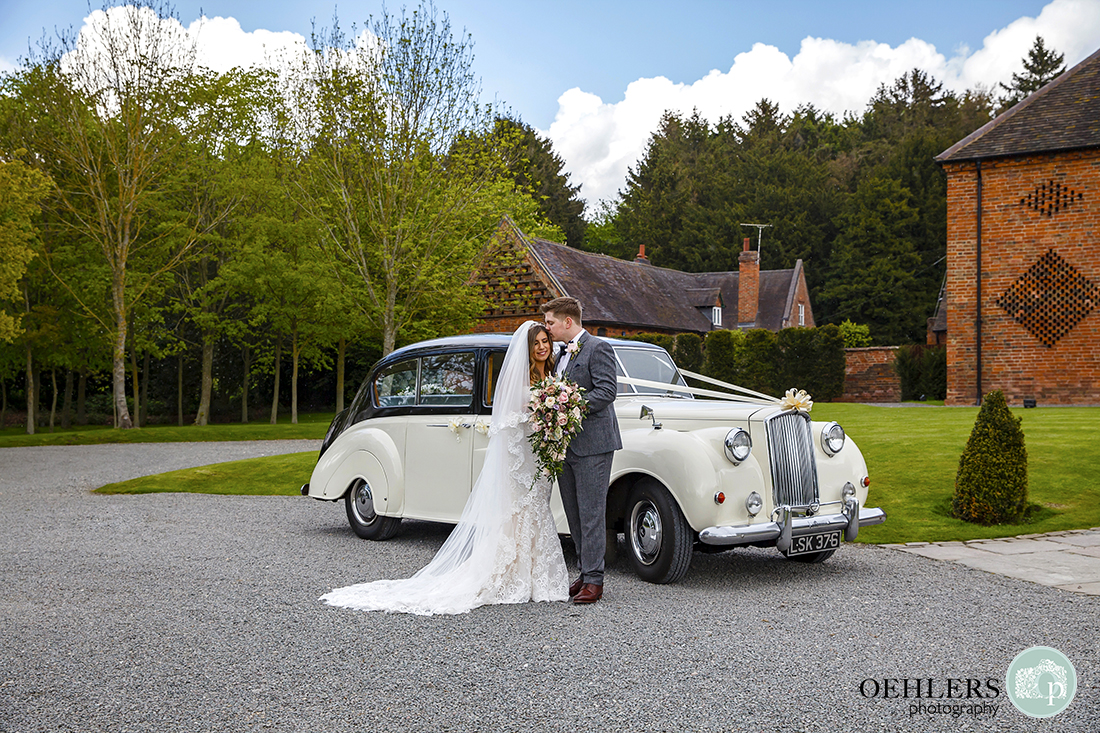 Shustoke Barn Wedding Photographers-Shot of the married couple, standing in front of the wedding car with groom kissing his bride's head.