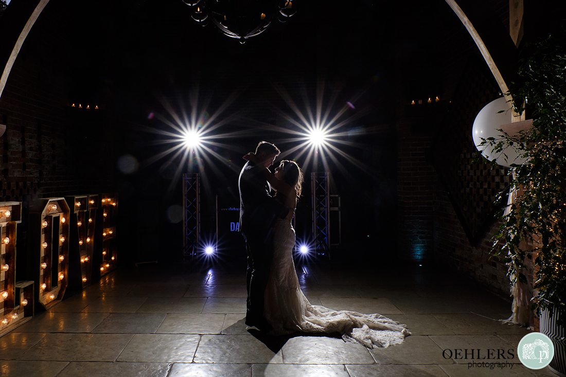 Shustoke Barn Wedding Photographers-Wedding couple doing their first dance illuminated by large love letters sign and starburst flash.