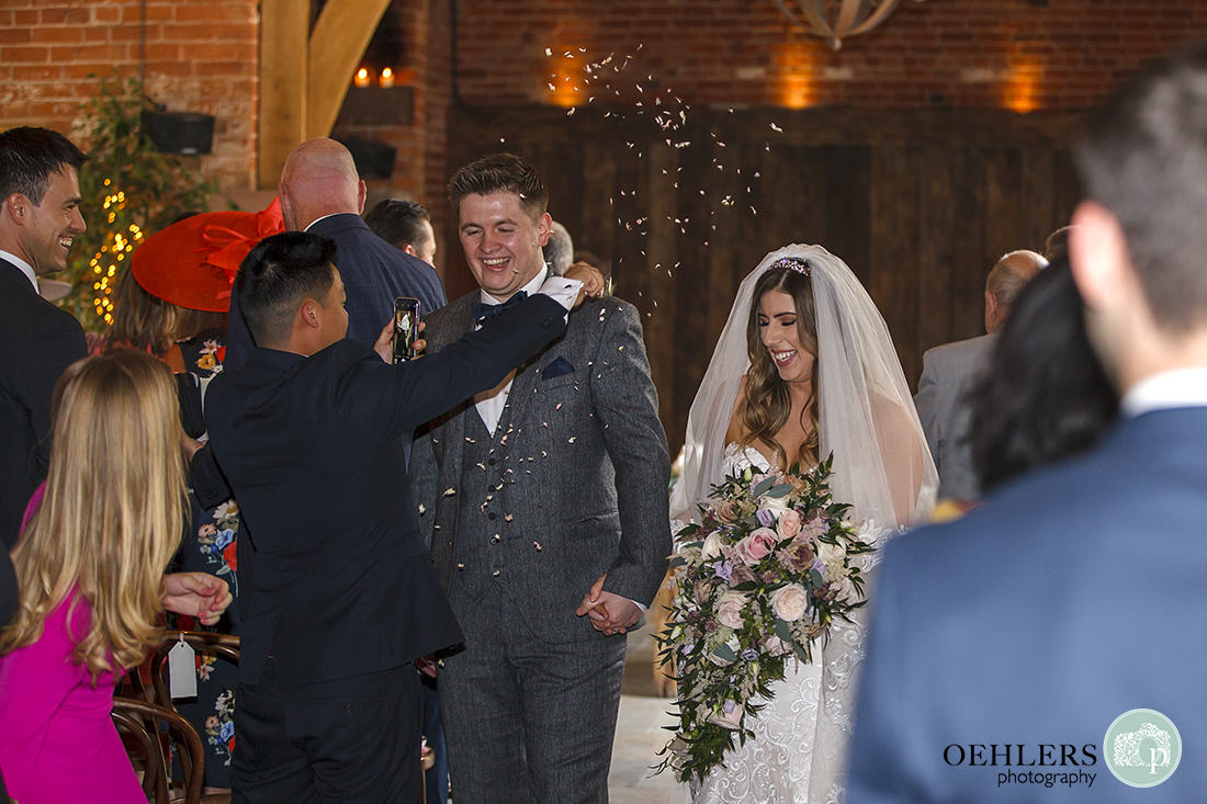 Shustoke Barn Wedding Photographers-Guest throwing confetti at the bride and groom as they walk back down the aisle.