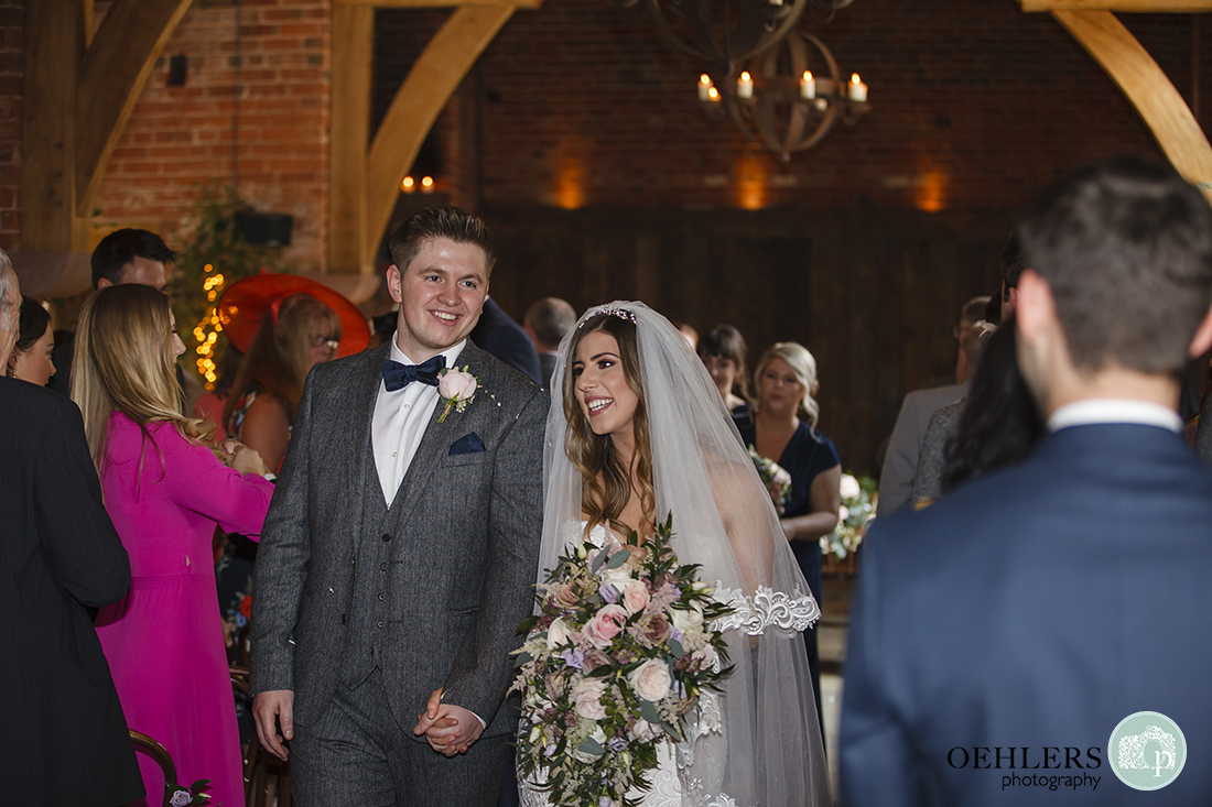 Shustoke Barn Wedding Photographers-Bride and groom with beaming smiles to their guests as they walk back down the aisle.