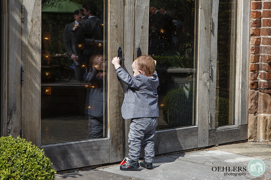 Shustoke Barn Wedding Photographers-Very young suited wedding guest, driven by hunger, makes an early dash for the doors of the wedding breakfast room.