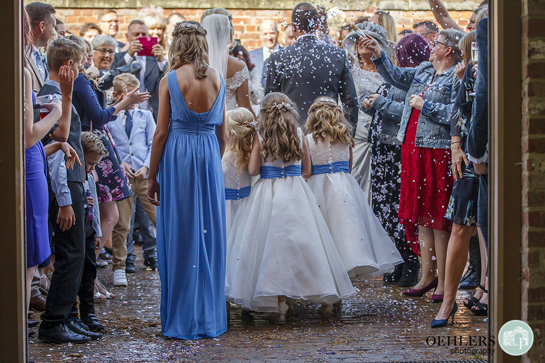 flower girls holding the bridal train as the couple walks outside through the confetti line