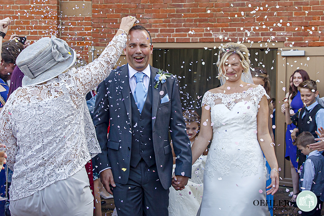 guest pouring confetti over the groom's head whilst bride screws up her face as confetti is chucked at her