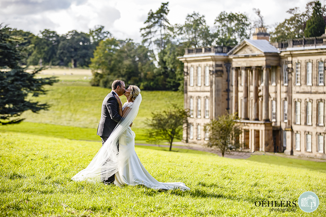 beautiful shot in the sunshine as the couple kisses with the fascade of Calke Abbey in the background