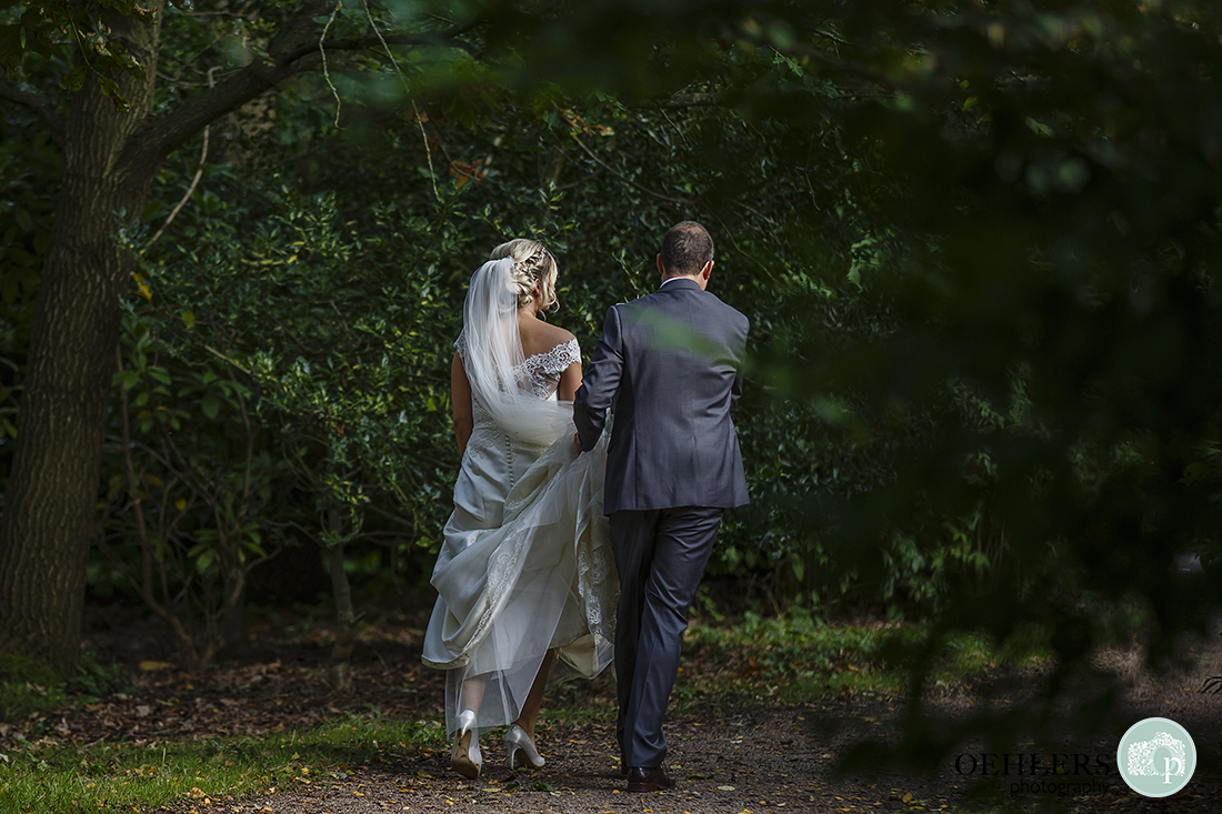 Groom carries the bride's train as they walk down a pathway