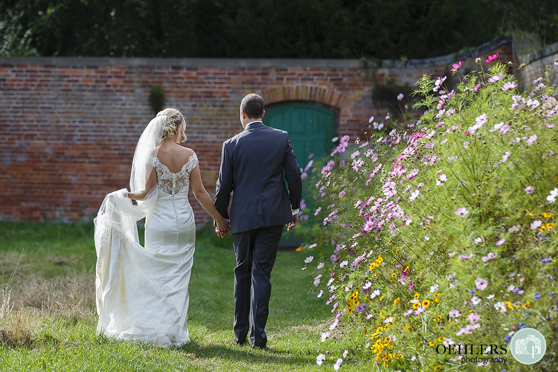 couple walking hand in hand away from the camera with bride holding her dress