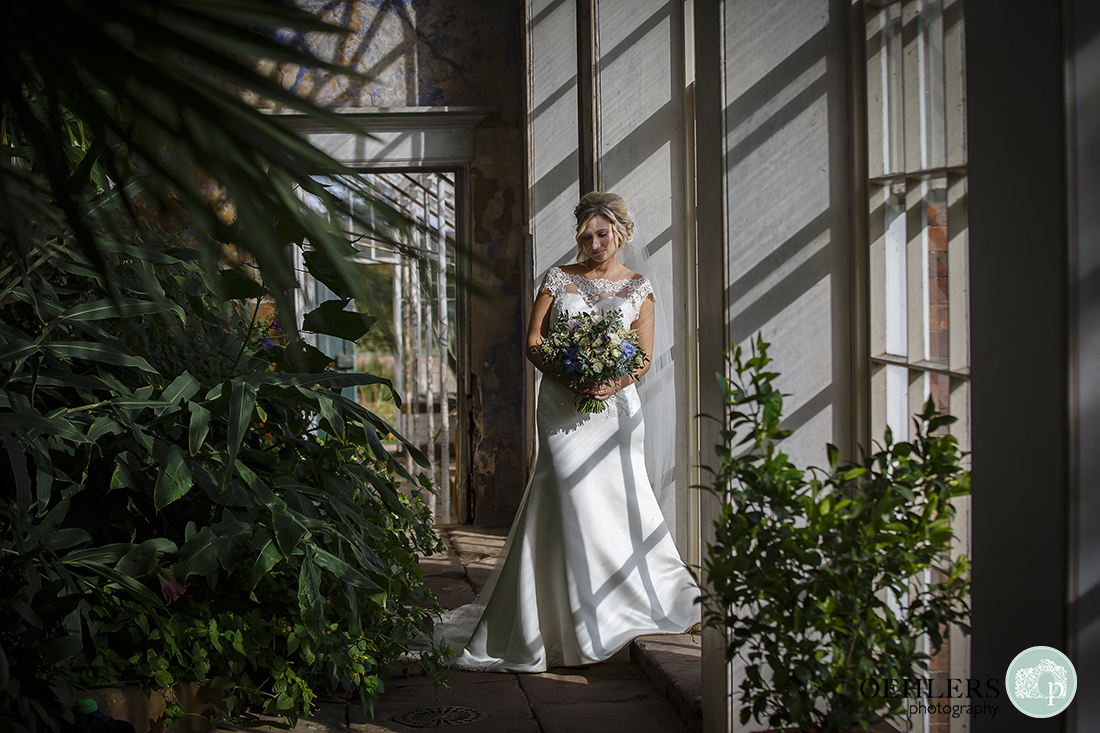 bride looking down at her bouquet whilst leaning against a pillar in the orangery