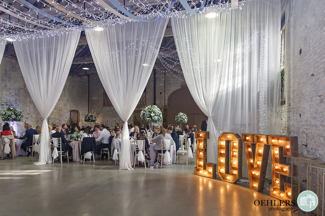 elegant wedding breakfast area adorned by fairy lights and voiles with love sign to the right