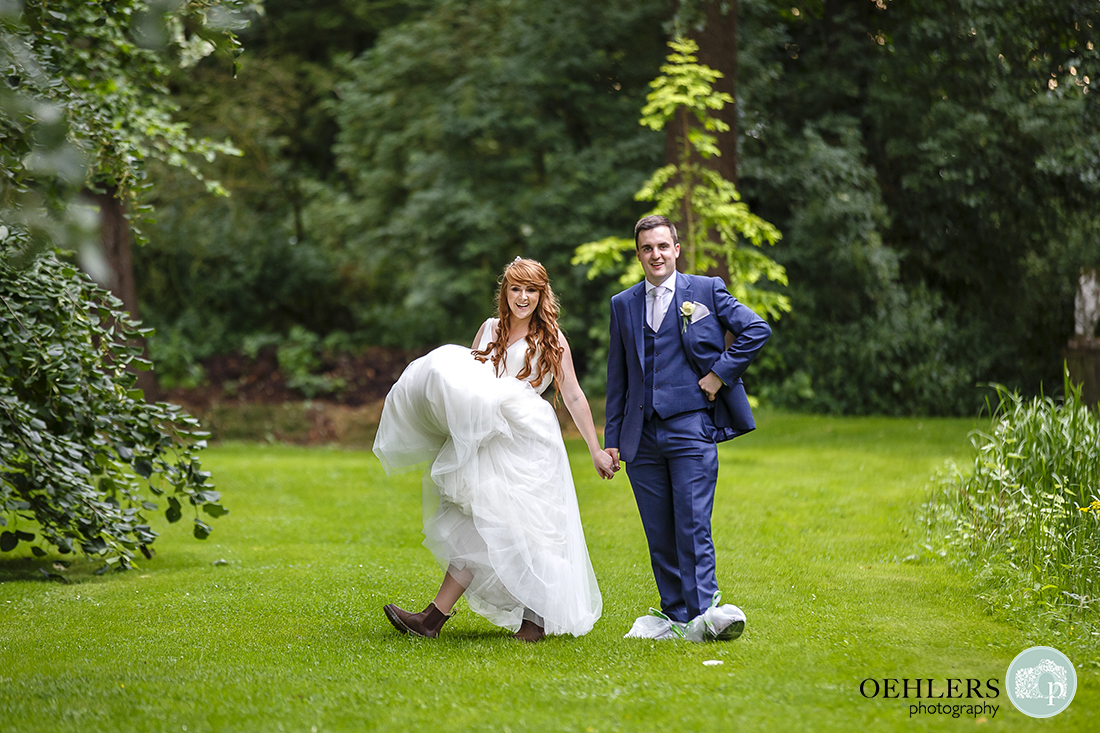 Funny photo of the Bride and Groom showing off their footwear with the groom wearing plastic bags around his shoes.