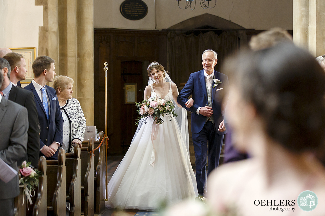 Bride, arm in arm with her dad spots her groom for the first time at the end of the aisle.