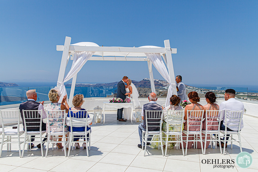 Santorini Destination Wedding Photographers - the first kiss as husband and bride under the canopy of the ceremony structure.