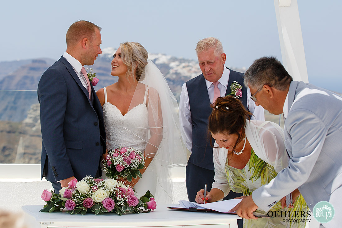 Mum witnessing the register whilst groom and bride look at each other and groom's dad looking over shoulder of mum.