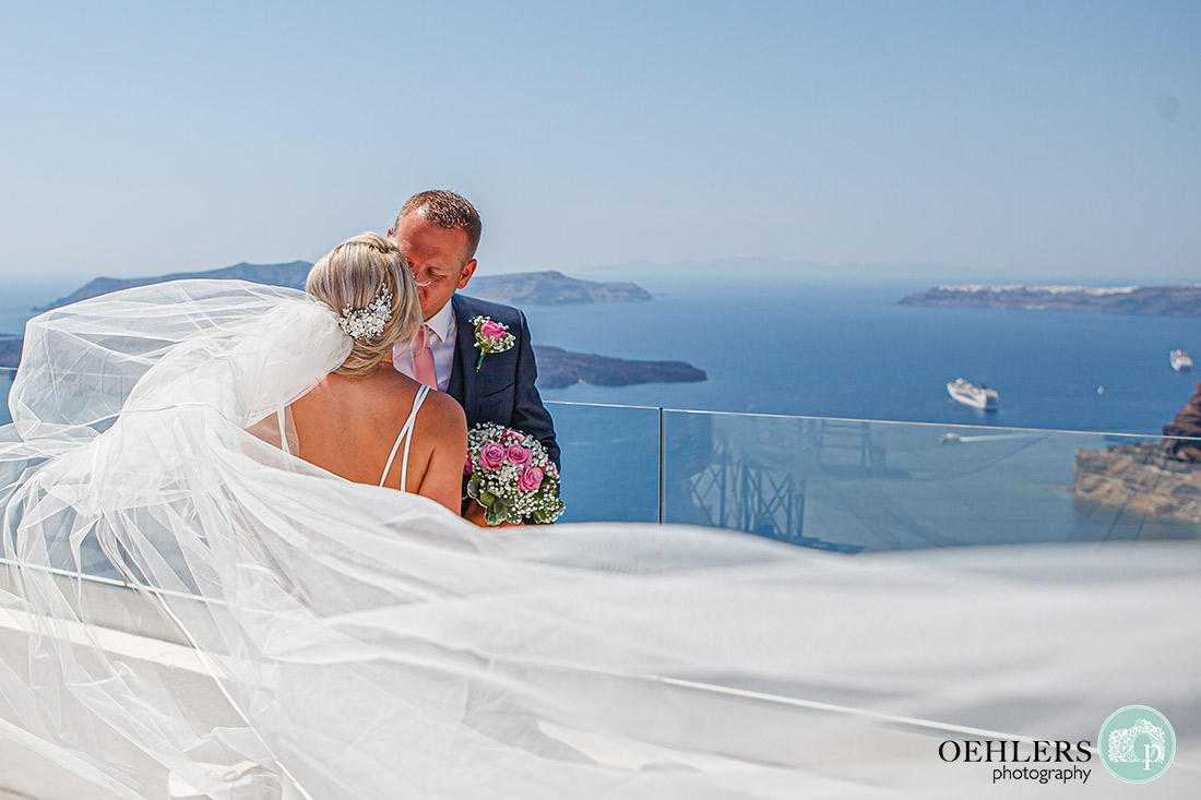 Santorini Destination Wedding Photographers - bride and groom kissing as veil spreads in between camera and them.
