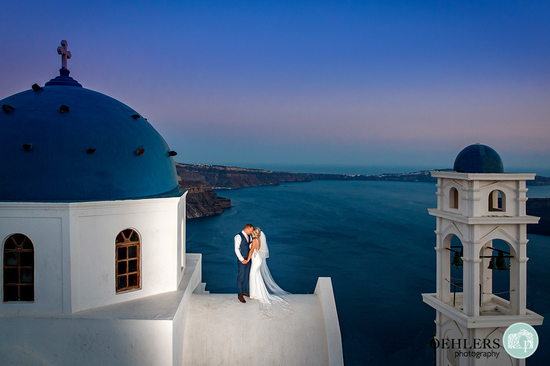 Destination Wedding Photographers - Santorini - bride and groom on top of a church in Imerovigli.