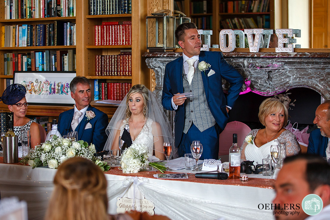 Groom making his speech at the top table with the bride pulling a face.
