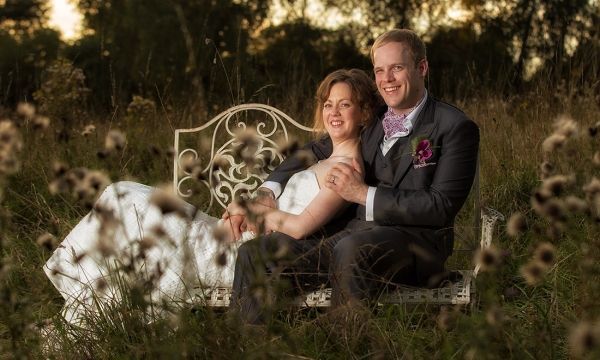 Bride and Groom sitting on a bench in the middle of a field.