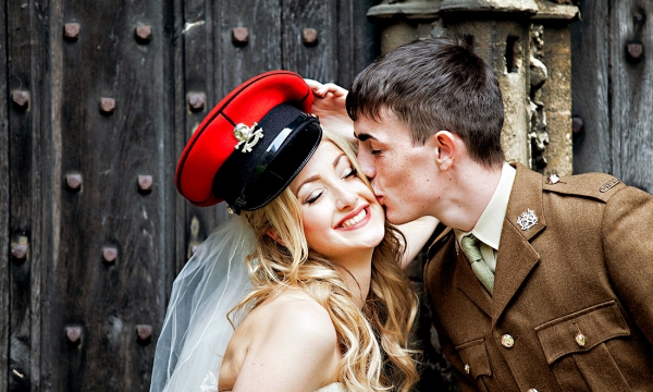 bride wears army cap whilst army grrom kisses her on the cheek