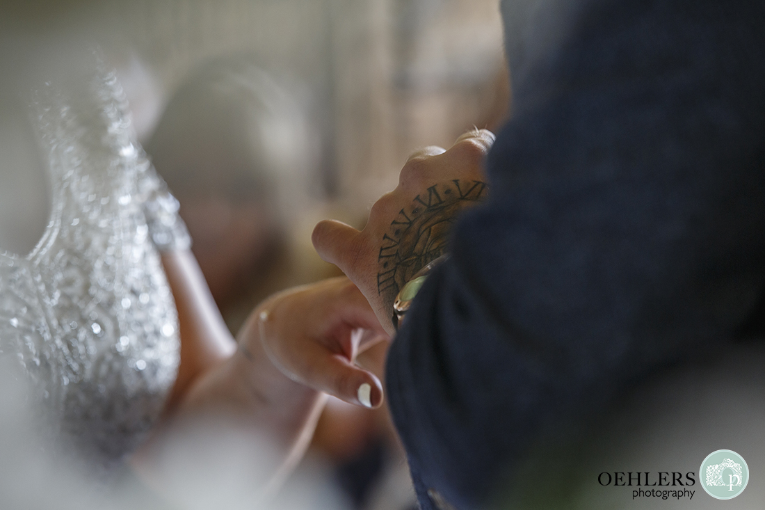 Wedding photographer at Prestwold - Close up of groom with tatooed hand putting the ring onto the bride's finger.