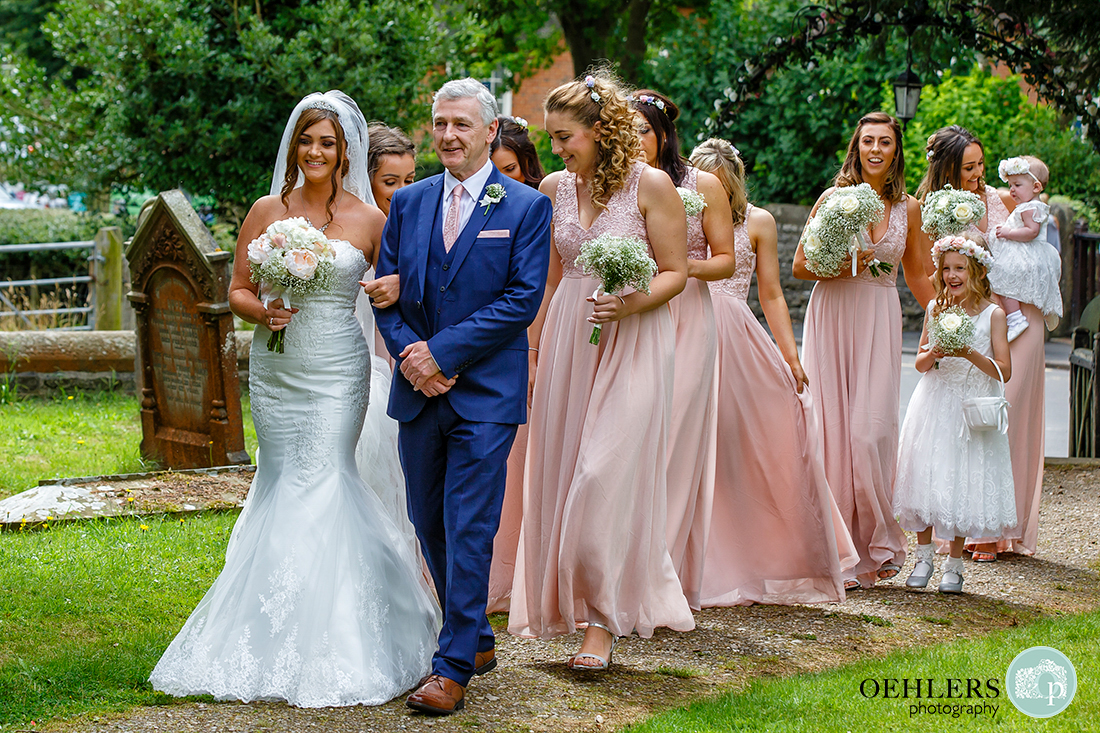 Osmaston Park wedding photography - St Martin's Church, Osmaston - Bride walking down pathway with dad and bridesmaids towards the church.