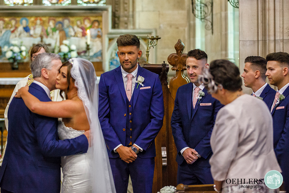 Osmaston Park wedding photography - Groom looks on as the bride kisses her dad as he hands her over to the groom.