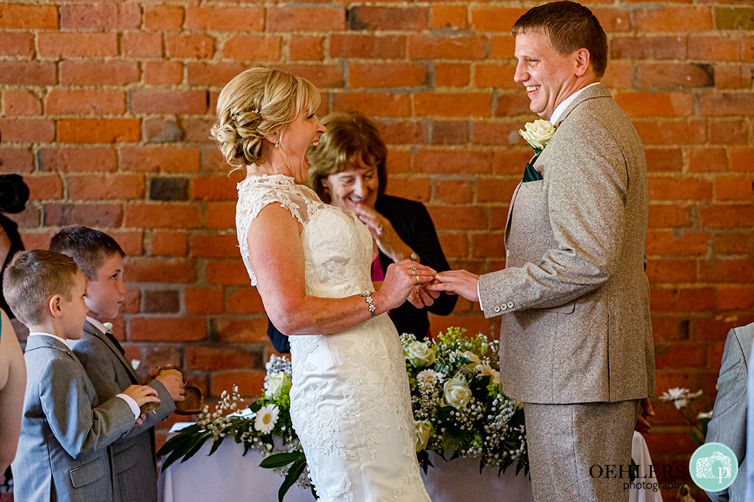 Bride laughing as she places the wedding ring on the groom's finger