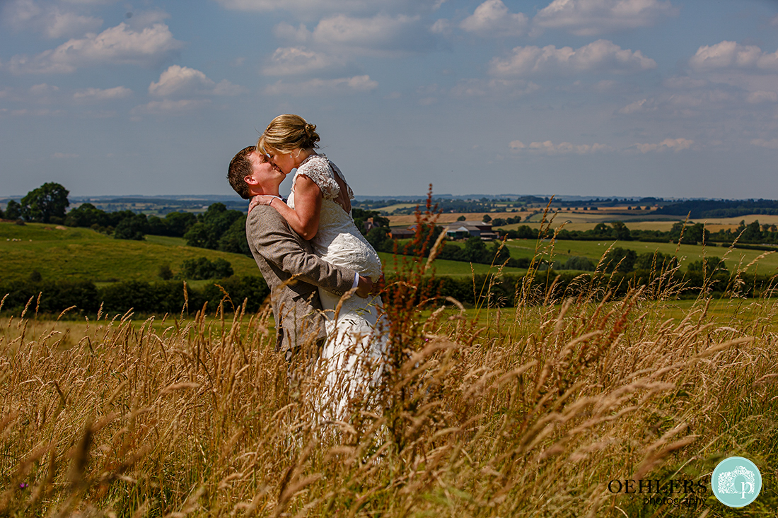 Groom lifts up the bride as they kiss in the wheat field