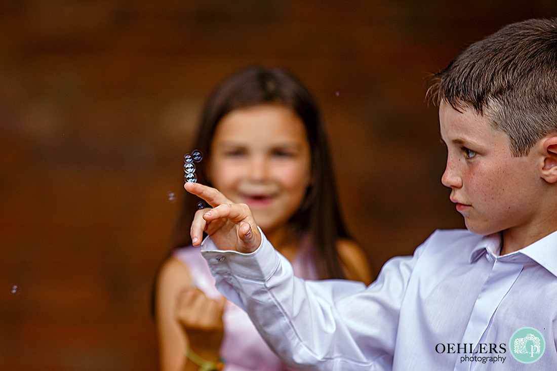 Young lad balancing several small bubbles on top of each other on his finger whilst a young girl looks on.