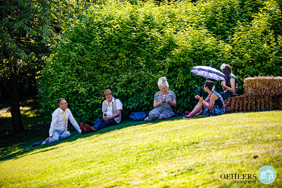 Guests sitting in the shade on a sloping lawn enjoying the sunshine